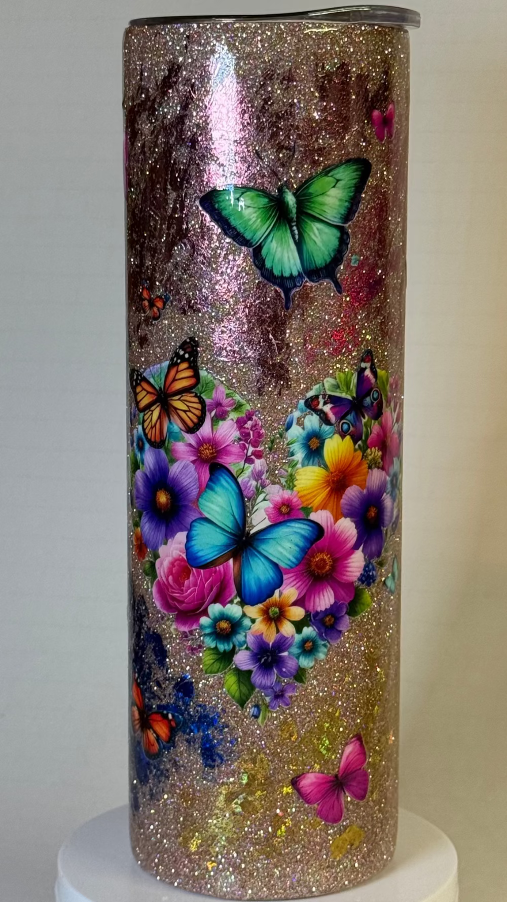 Tumbler with glittery surface and colorful butterfly and flower design on a neutral background